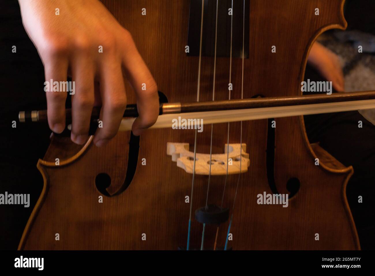 dettaglio di una mano che tiene un arco musicale per suonare un violoncello e per far uscire il suono con messa a fuoco selettiva Foto Stock