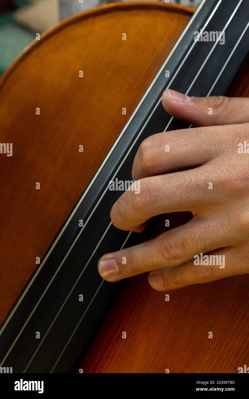 dettaglio di una mano posta sul collo di un violoncello per suonare una nota musicale con messa a fuoco selettiva Foto Stock