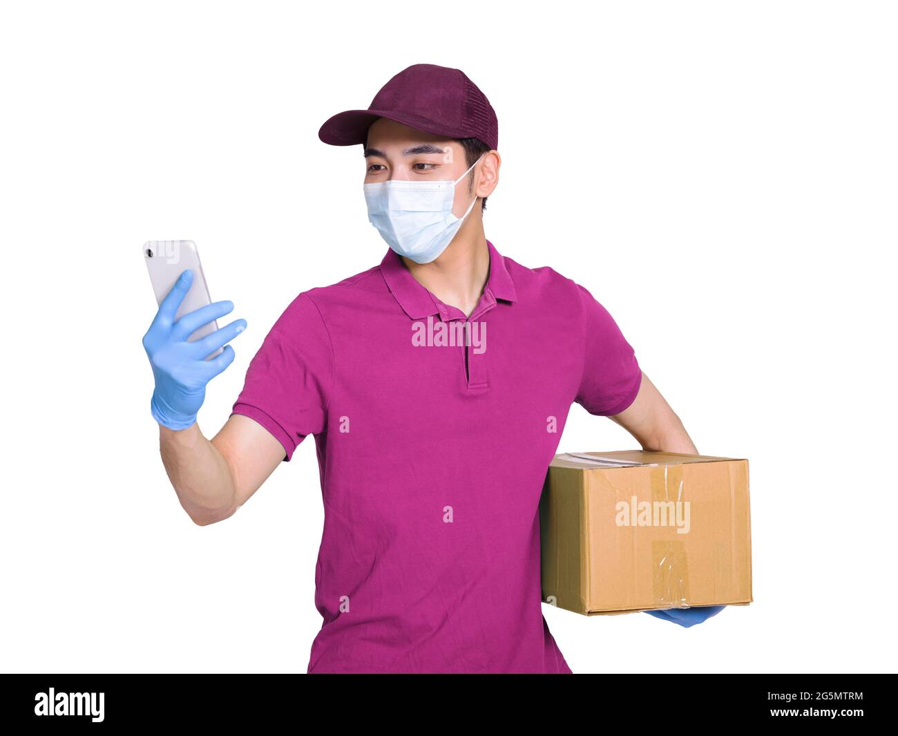 Giovane corriere che indossa abiti e cappelli rossi, indossando maschere e guanti per proteggersi, lavorando durante l'epidemia di covid-19, controllando gli smartphone t Foto Stock