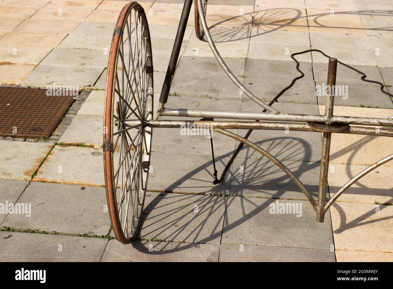 La ruota di un carro e la sua ombra su un marciapiede lastricato Foto Stock