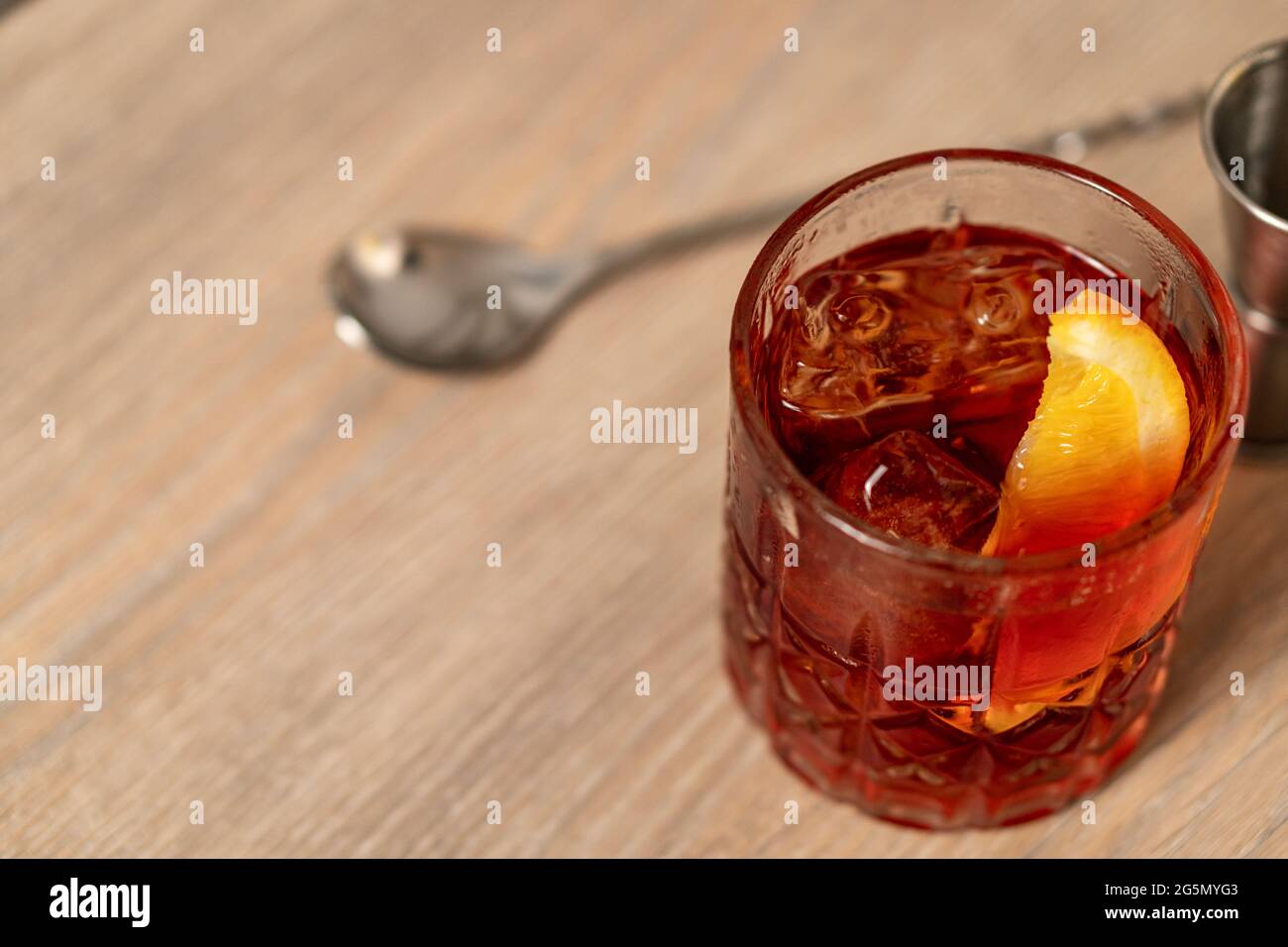 Vista panoramica del cocktail negroni con zeppa arancione su superficie in legno con cucchiaio di miscelazione Foto Stock