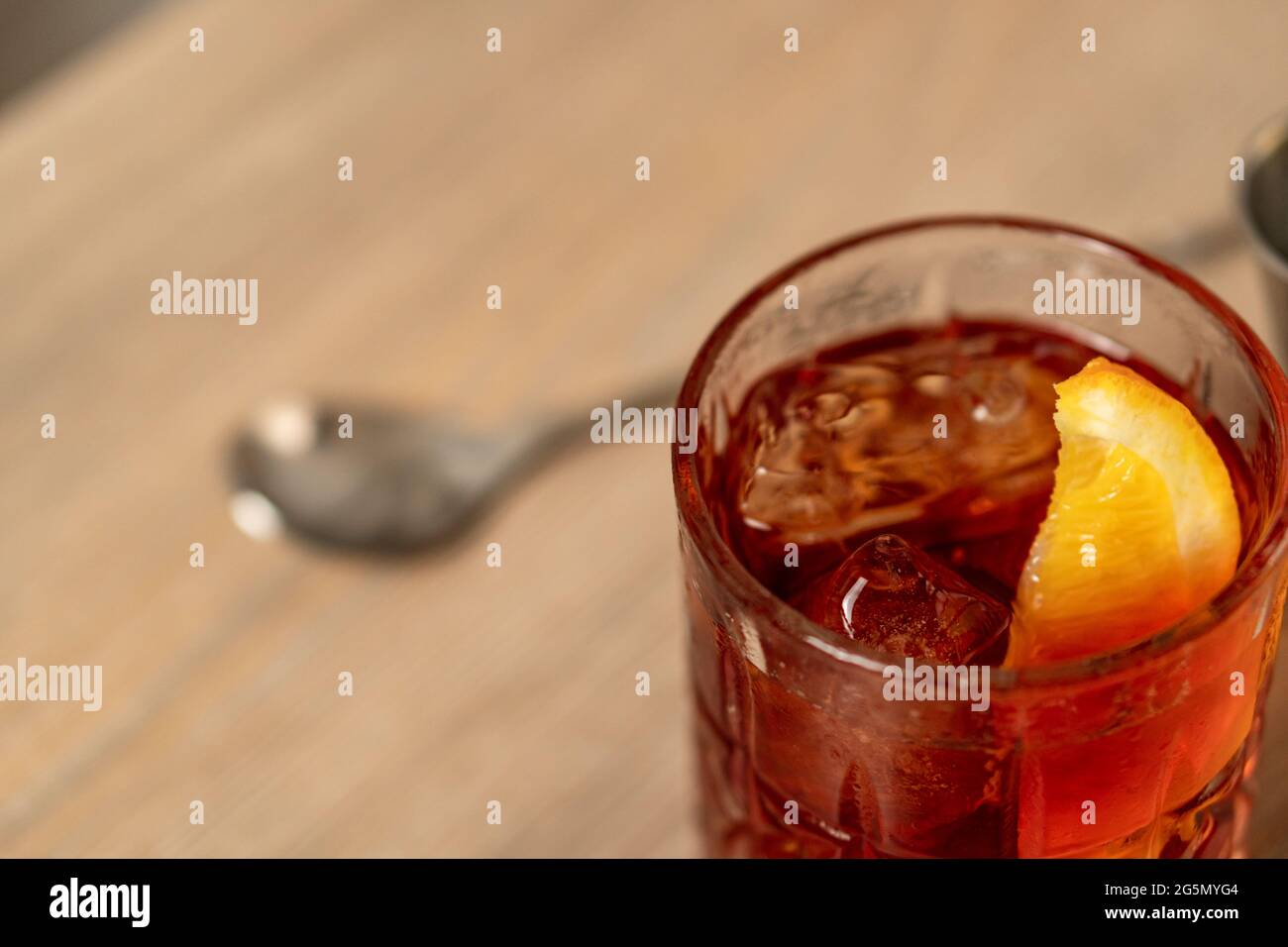 Vista ravvicinata del cocktail negroni con zeppa arancione su superficie in legno con cucchiaio di miscelazione Foto Stock