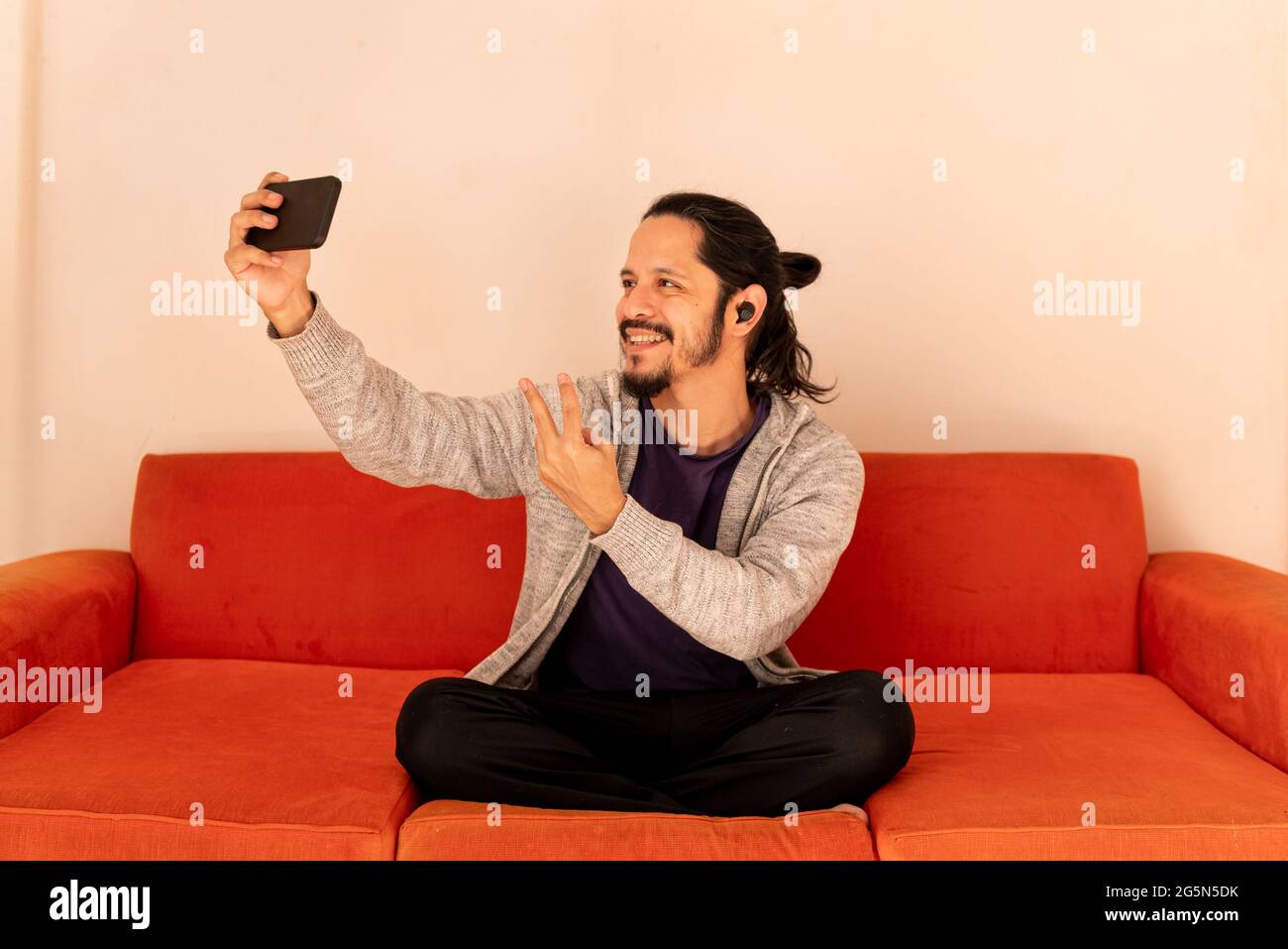 Giovane uomo che usa lo smartphone portando un selfie a casa nel salotto Foto Stock