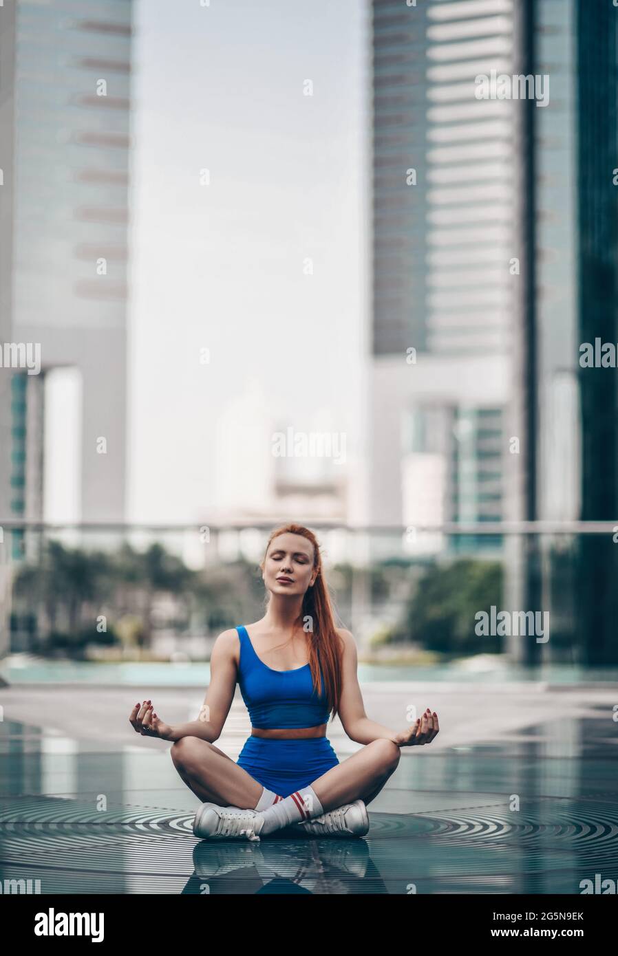 Donna yoga sottile in pantaloncini sportivi e top siede in posizione lotus, asana con gambe incrociate sulla strada della città di Dubai Foto Stock