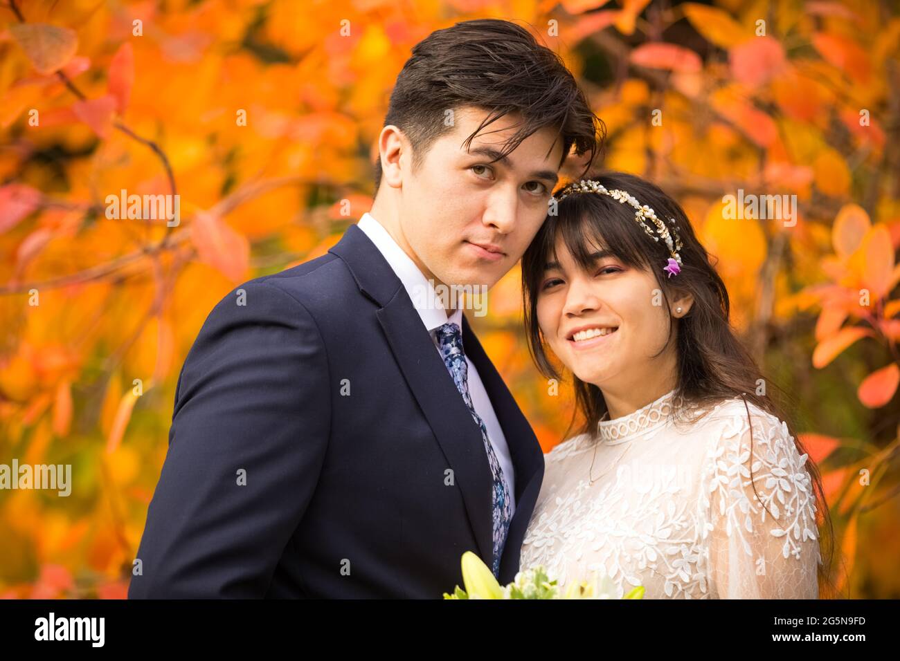 Sposa biraciale e sposo insieme all'aperto dopo il matrimonio autunnale con brillanti foglie arancioni colorate sullo sfondo Foto Stock