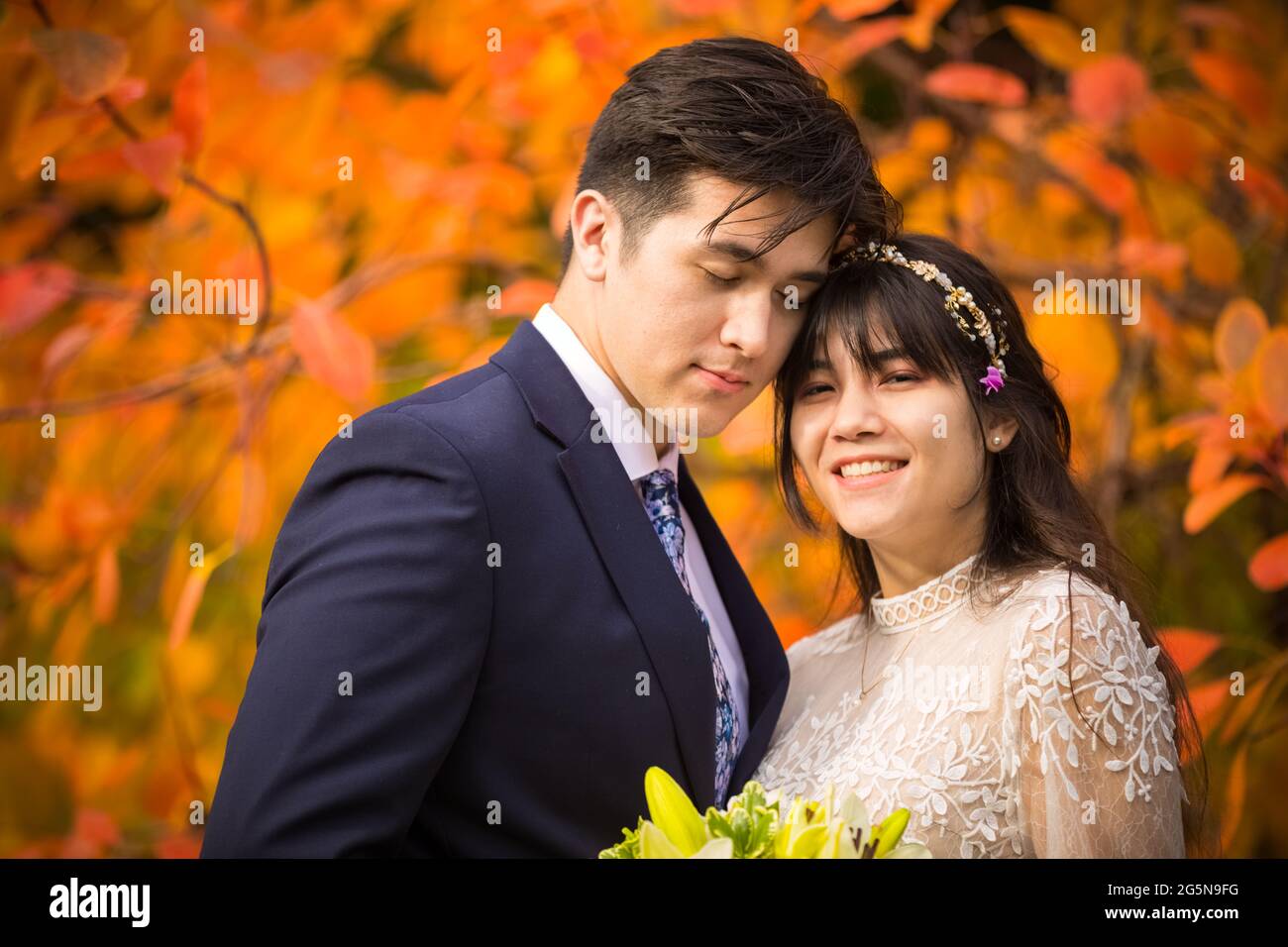 Sposa biraciale e sposo insieme all'aperto dopo il matrimonio autunnale con brillanti foglie arancioni colorate sullo sfondo Foto Stock