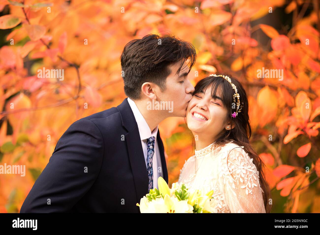 Biracial sposata coppia appena sposata baciando all'aperto da brillanti foglie arancioni d'autunno Foto Stock