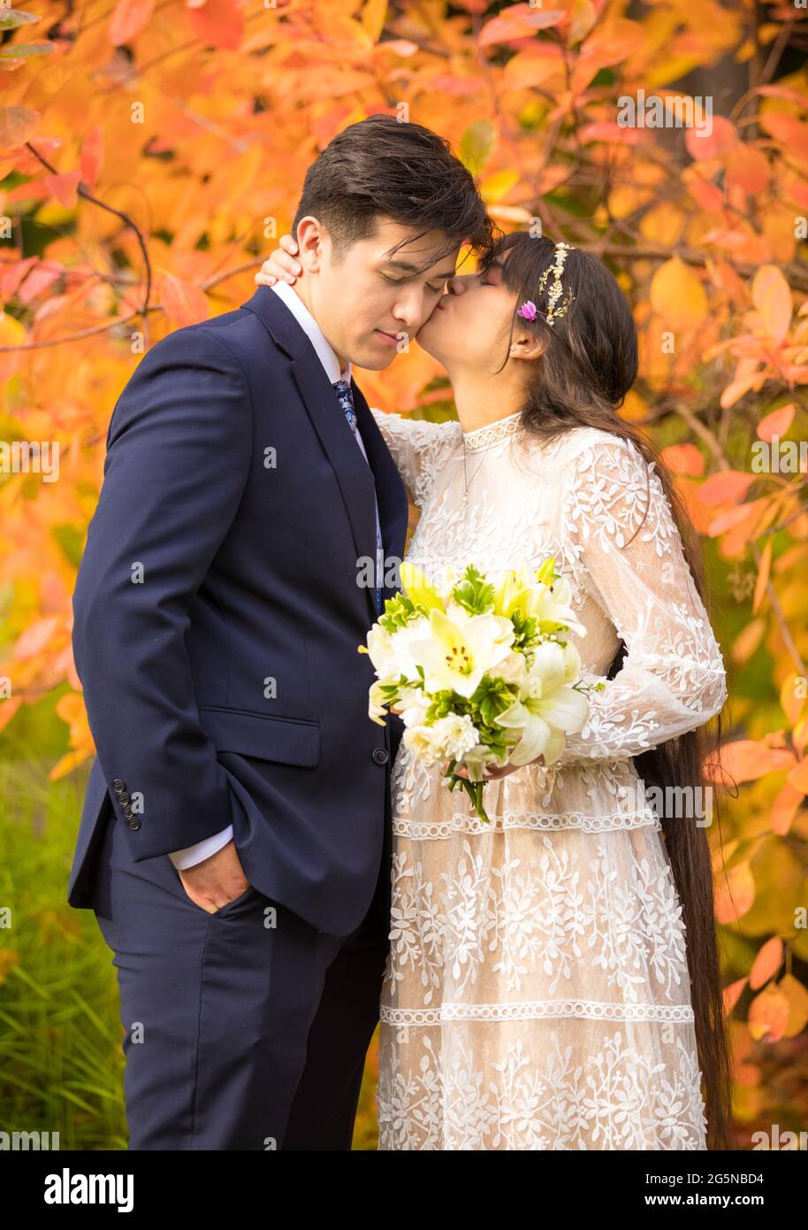 Biracial sposata coppia appena sposata baciando all'aperto da brillanti foglie arancioni d'autunno Foto Stock