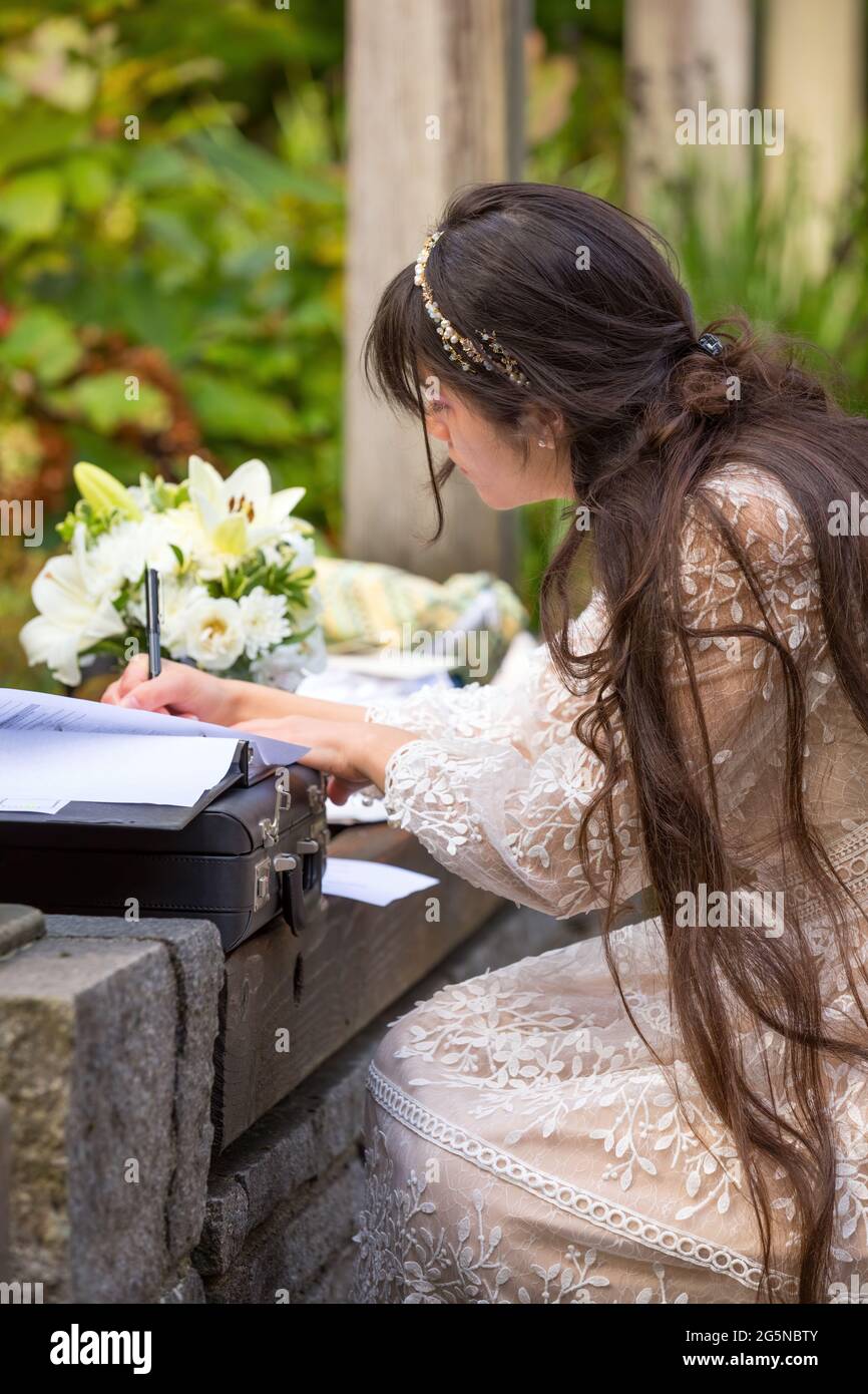 Nuova sposa biraciale che si inginocchiò fino a firmare il certificato di matrimonio dopo il matrimonio all'aperto Foto Stock