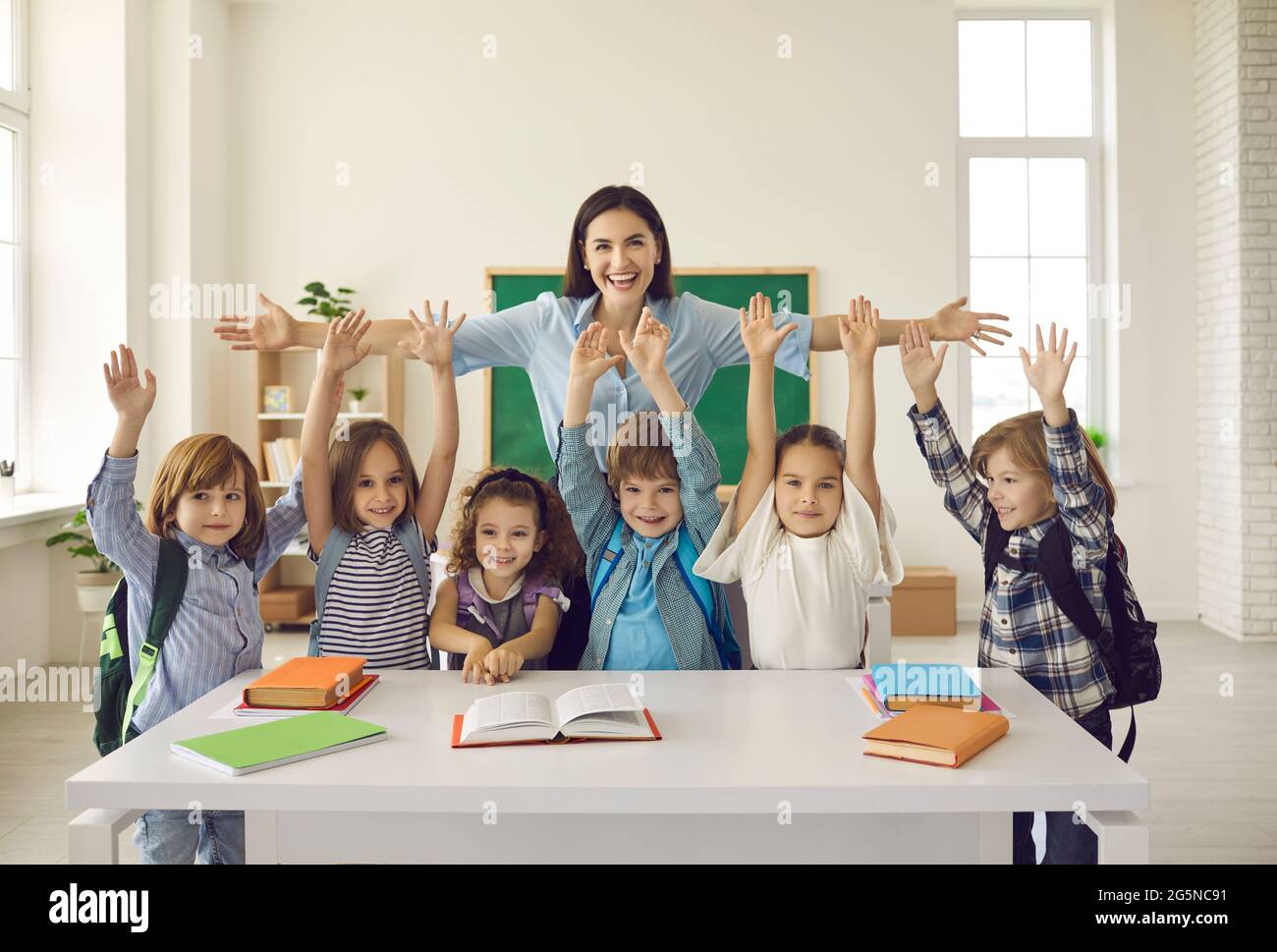 Insegnante felice con le armi ampiamente diffuse per abbracciare i bambini allegri alzando le mani Foto Stock