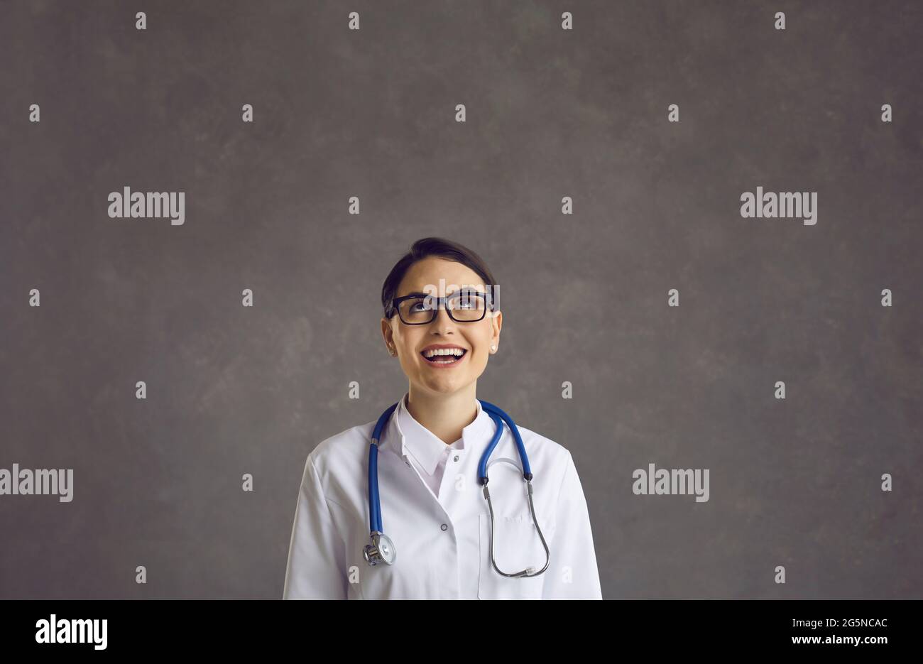 Ritratto di felice dottore femminile guardando in su, pensando a qualcosa di divertente e ridendo Foto Stock