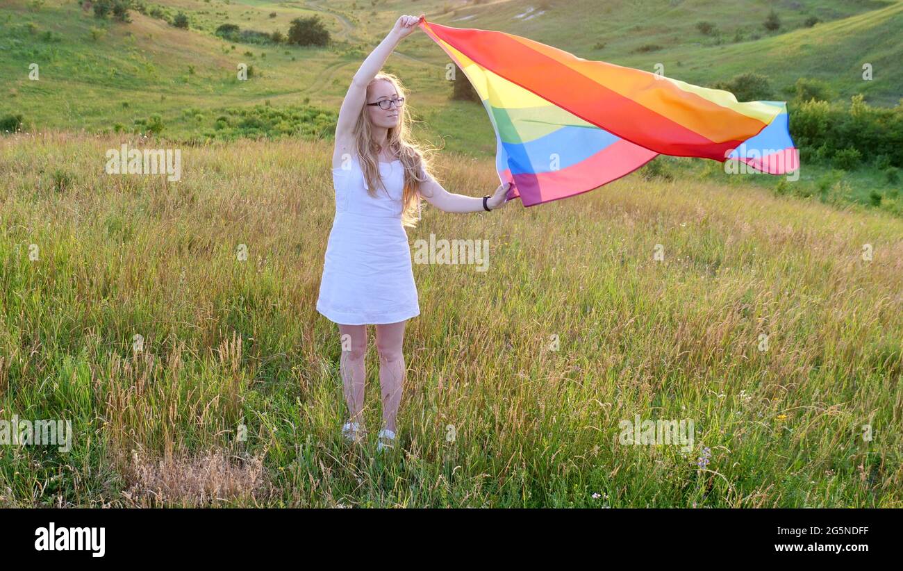 Bisessuale, lesbica, donna, persona, omosessuale tiene la bandiera di LGBT sulle colline verdi su un tramonto di giorno soleggiato e festeggiando una parata gay, il giorno di bisessualità o il giorno nazionale che esce nel mese dell'orgoglio Foto Stock