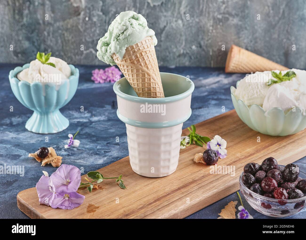 Ancora vita con pistacchio e gelato cremoso in vasi e cono su sfondo blu Foto Stock