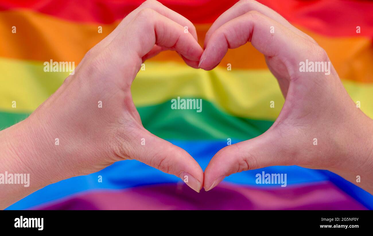 Giovane coppia lesbica che tiene le mani sul cuore a forma di arcobaleno LGBT bandiera sfondo. La coppia omosessuale femminile celebra il mese della dignità, il giorno della bisessualità Foto Stock