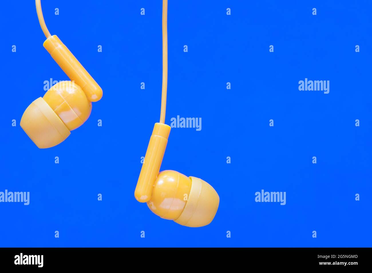 Gli auricolari di colore arancione si vestiscono su uno sfondo blu chiaro con spazio per la copia. Concetto di tecnologia audio. Foto Stock