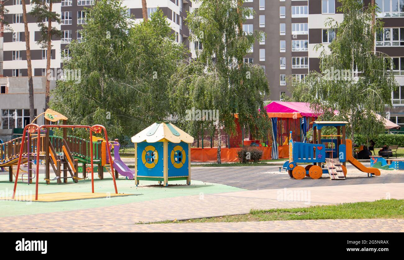 Un colorato e moderno parco giochi nel cortile in un parco senza persone. Swing, carosello esterno per bambini. Un parco giochi in un parco pubblico circondato Foto Stock
