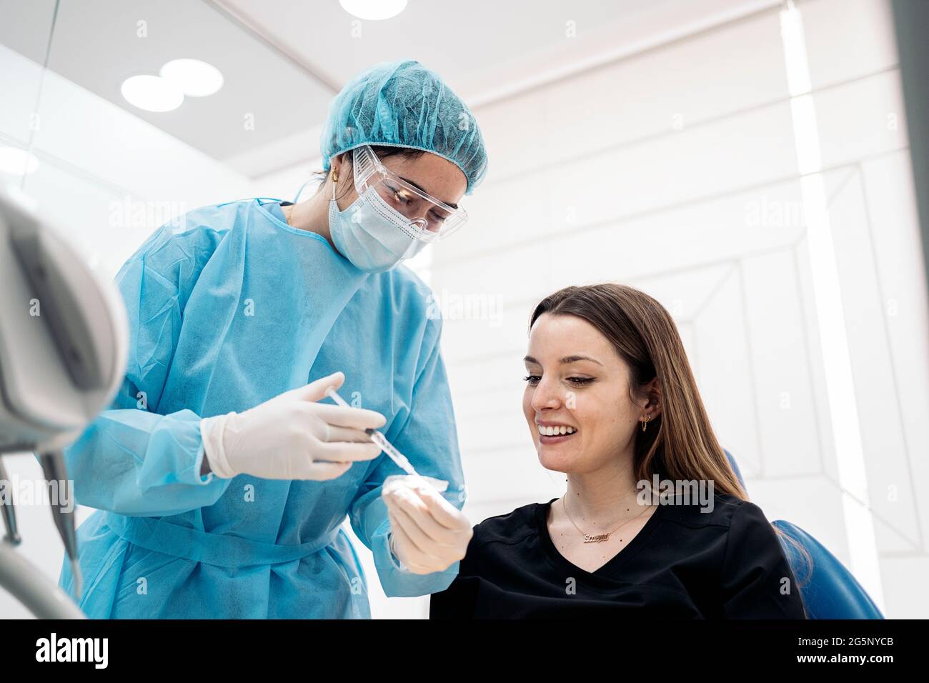 Dentista che indossa una maschera facciale e speciali indumenti protettivi  che spiegano al paziente come usare i copri denti Foto stock - Alamy