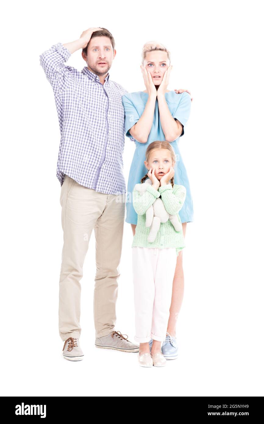 Immagine verticale a lunghezza intera di uomo e donna moderni in piedi con la loro figlia piccola stupita a qualcosa, sfondo bianco Foto Stock
