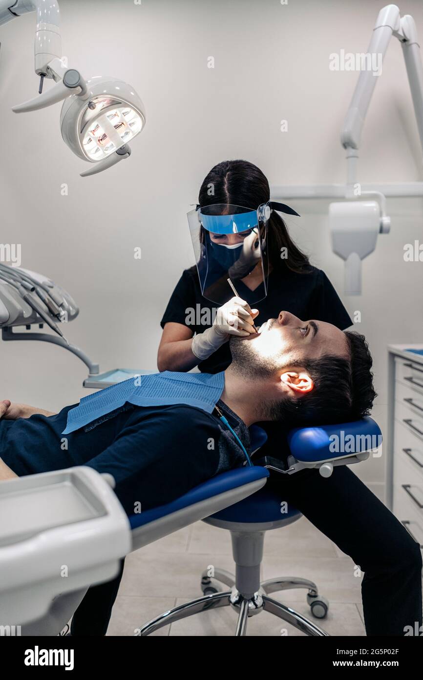 Dentista femminile che indossa una maschera protettiva per il viso  lavorando con il giovane uomo durante la revisione del check-up Foto stock  - Alamy