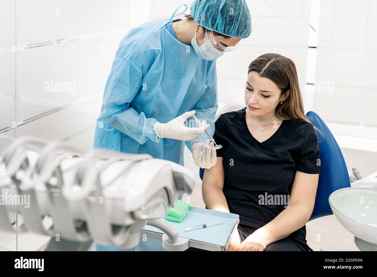 Dentista che indossa una maschera facciale e speciali indumenti protettivi  che spiegano al paziente come usare i copri denti Foto stock - Alamy