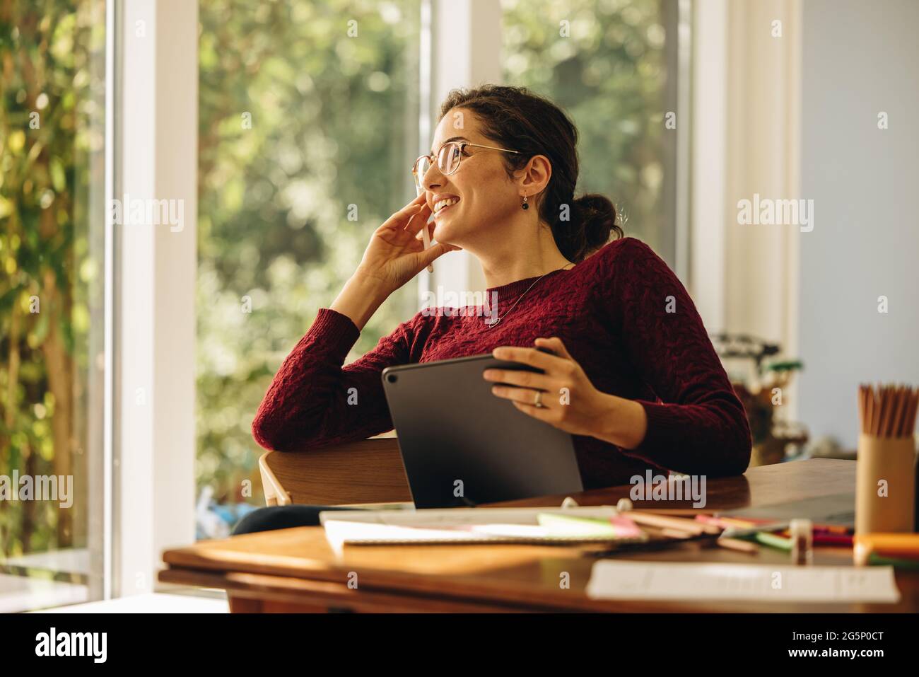 Donna di design seduta con tablet digitale che guarda lontano con la mano sul mento. L'artista pensa a nuove idee mentre lavora alle illustrazioni. Foto Stock