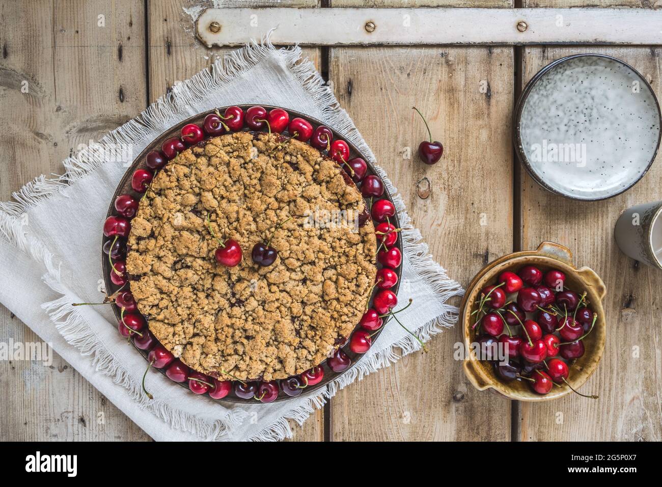 Torta di ciliegie con spolverini, ciliegia crumble, e una ciotola con ciliegie fresche su un rustico sfondo di legno, vista dall'alto Foto Stock