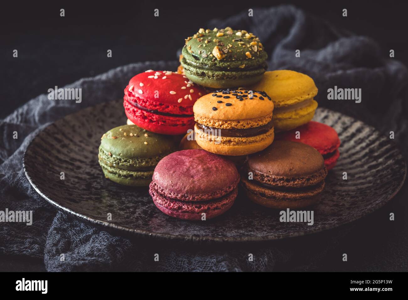 Macaron francesi colorati su un piatto scuro su sfondo nero Foto Stock