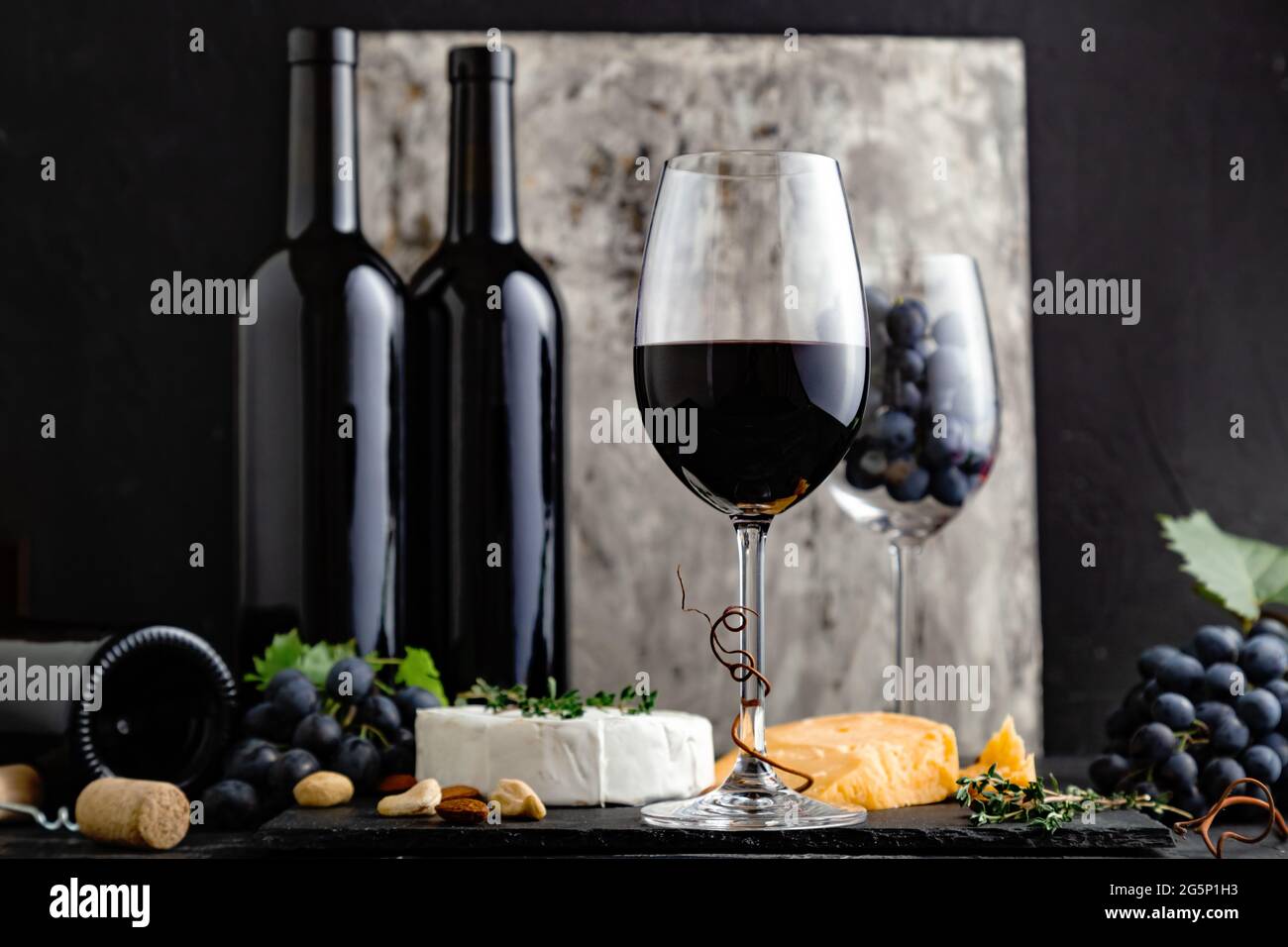 Vino rosso in vetro classico con composizione di bottiglie di vino. Elegante menu' Wine bar con spuntini, formaggio su sfondo scuro. Vino Rosso Vintage su nero Foto Stock