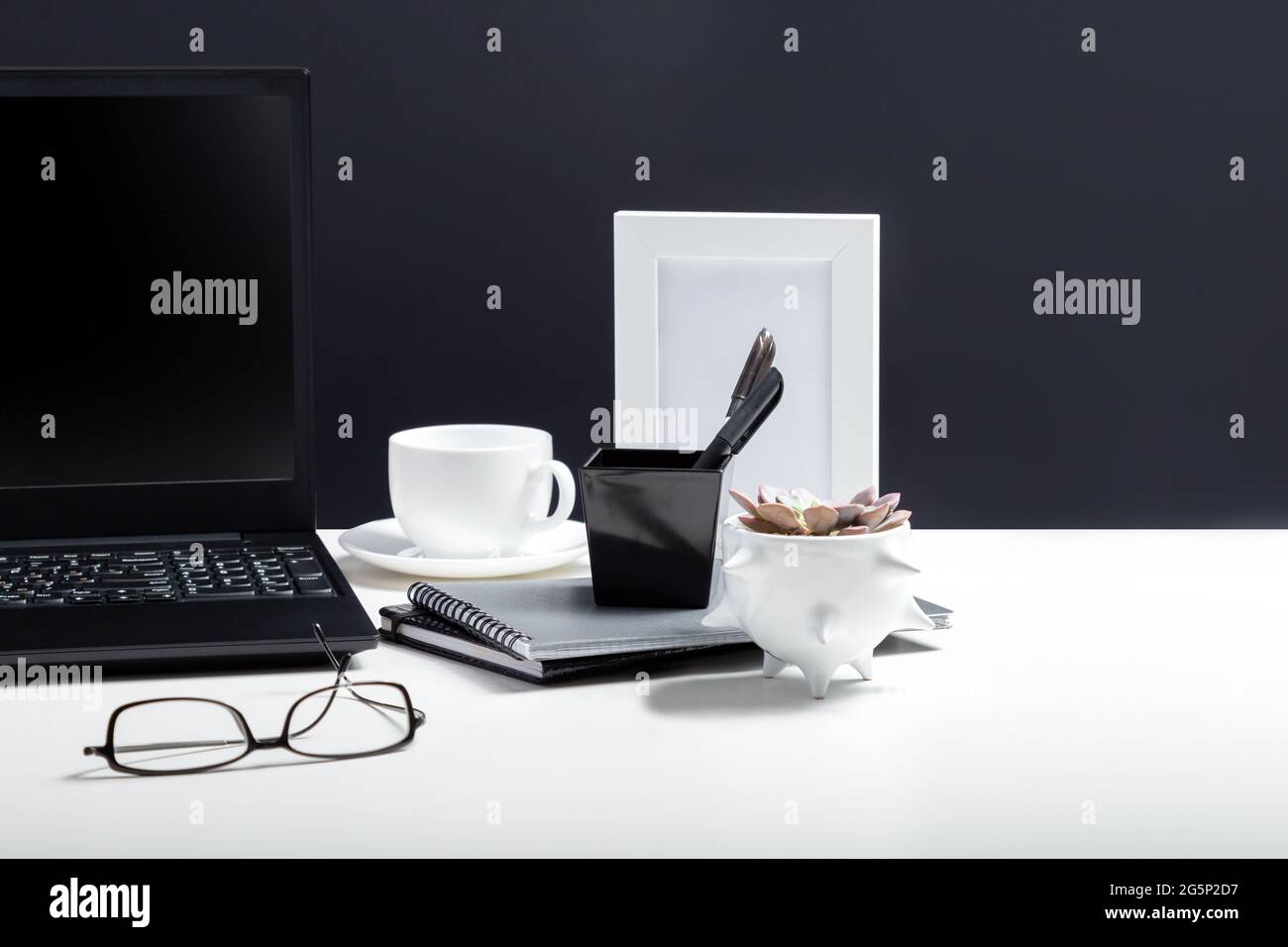 Tavolo bianco con computer portatile per lavoro o studio remoto. Notebook nero con modello di layout del display vuoto su sfondo nero. Area di lavoro scrivania PC ufficio in Foto Stock