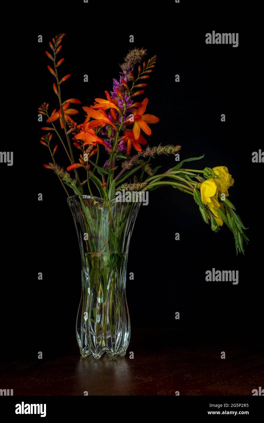 Vaso in vetro con sfondo nero di riferimento per fiori gialli e arancioni Foto Stock