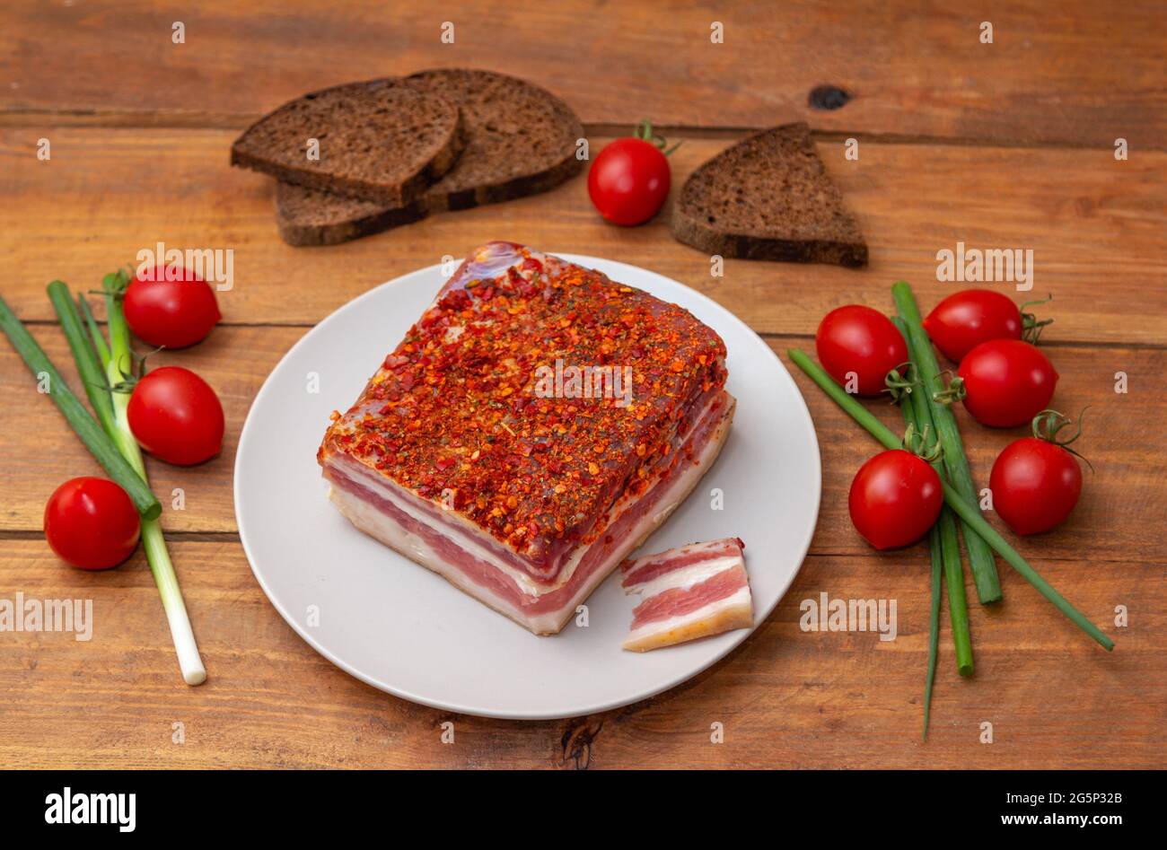 Pancetta piccante affumicata su un piatto. Fetta di carne di maiale affumicata su pane, pomodori ciliegini e cipolla verde su tavola di legno. Foto Stock