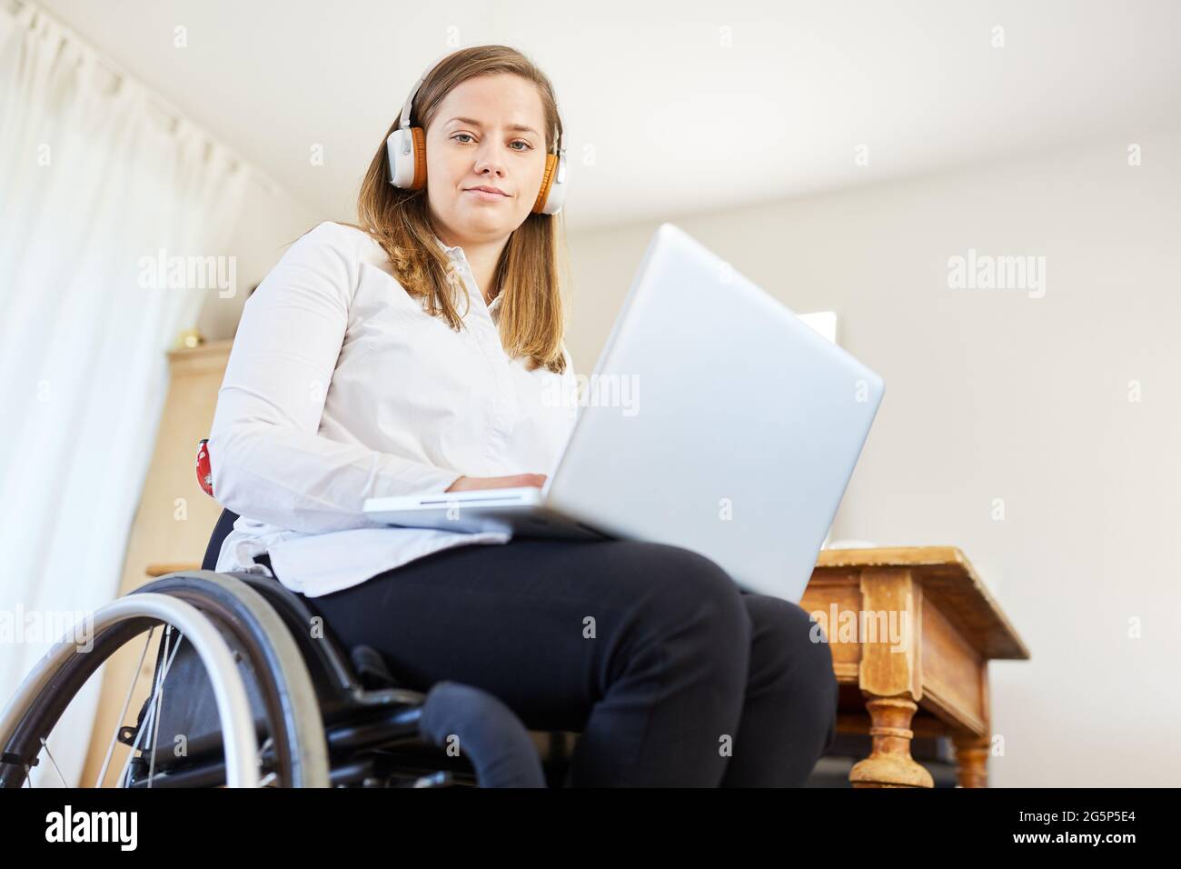 Donna con disabilità in sedia a rotelle che utilizza un computer portatile in ufficio durante una videoconferenza Foto Stock