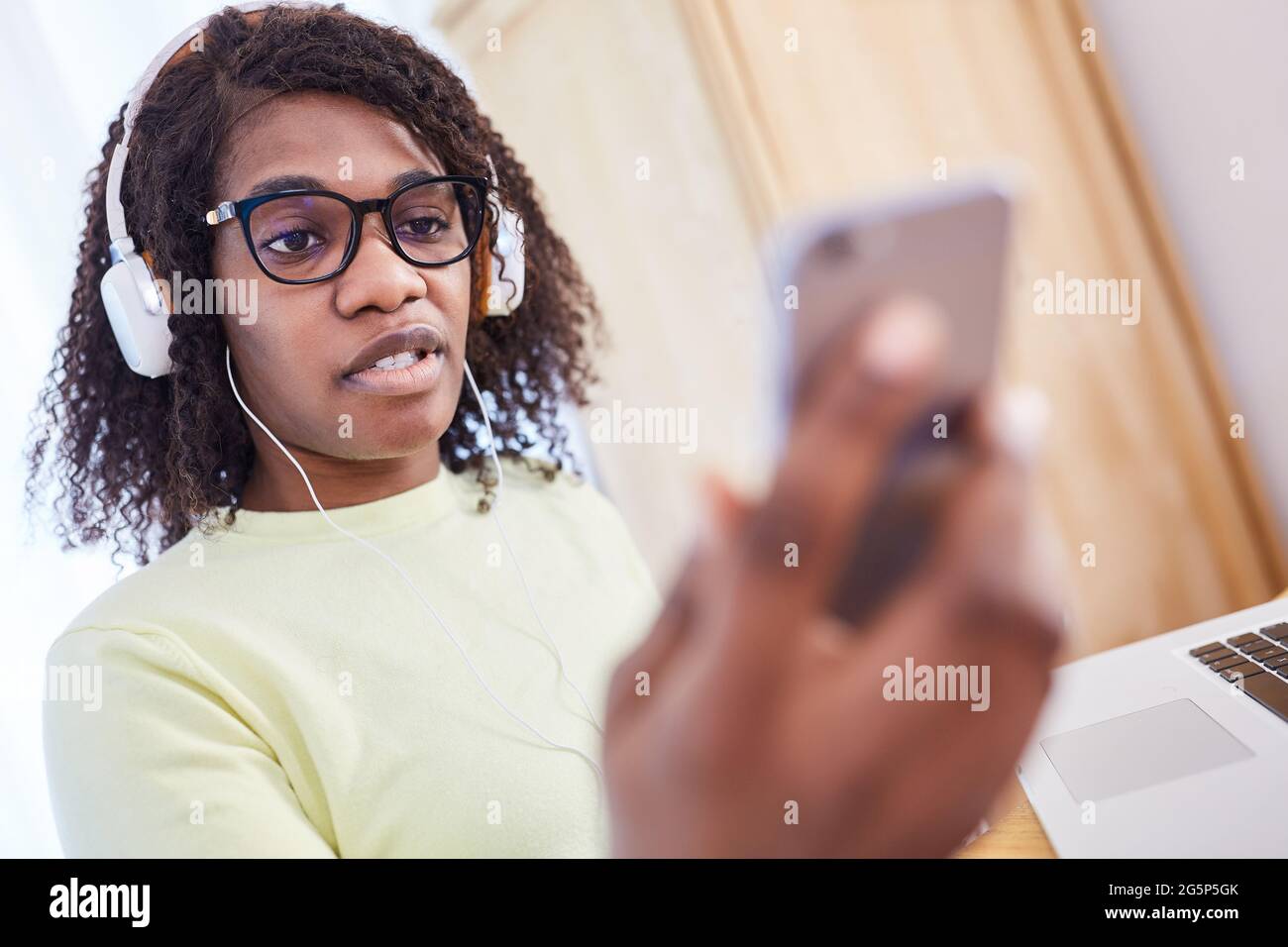 Donna d'affari afro-americana come freelance con smartphone e cuffie durante una chat video Foto Stock