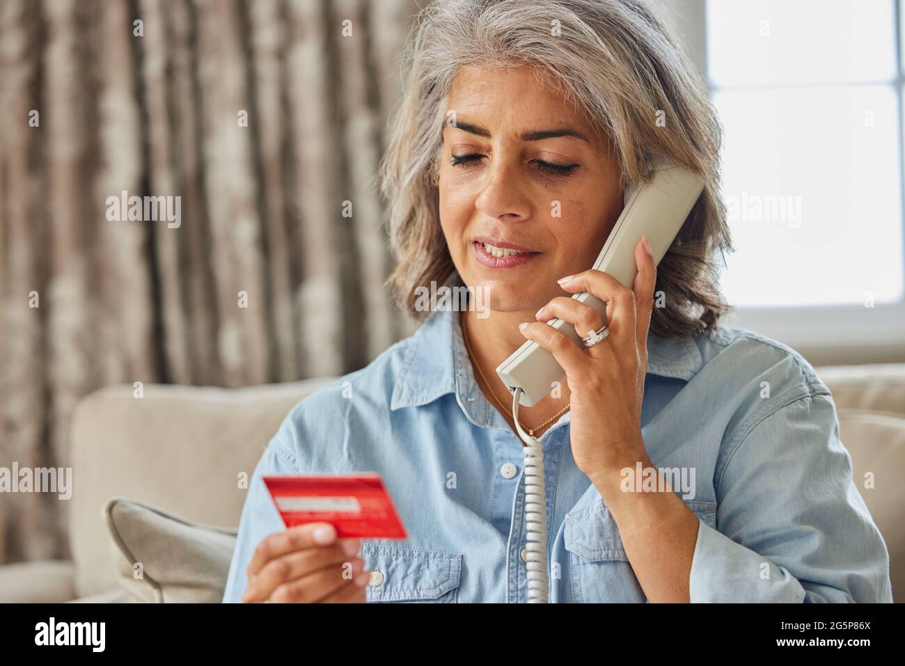 Donna matura a casa dando i dettagli della carta di credito sul telefono Foto Stock