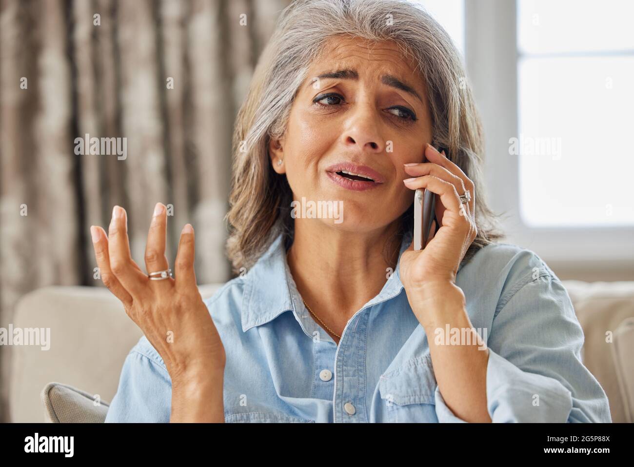 Donna matura frustrato che riceve una chiamata telefonica indesiderata a casa Foto Stock
