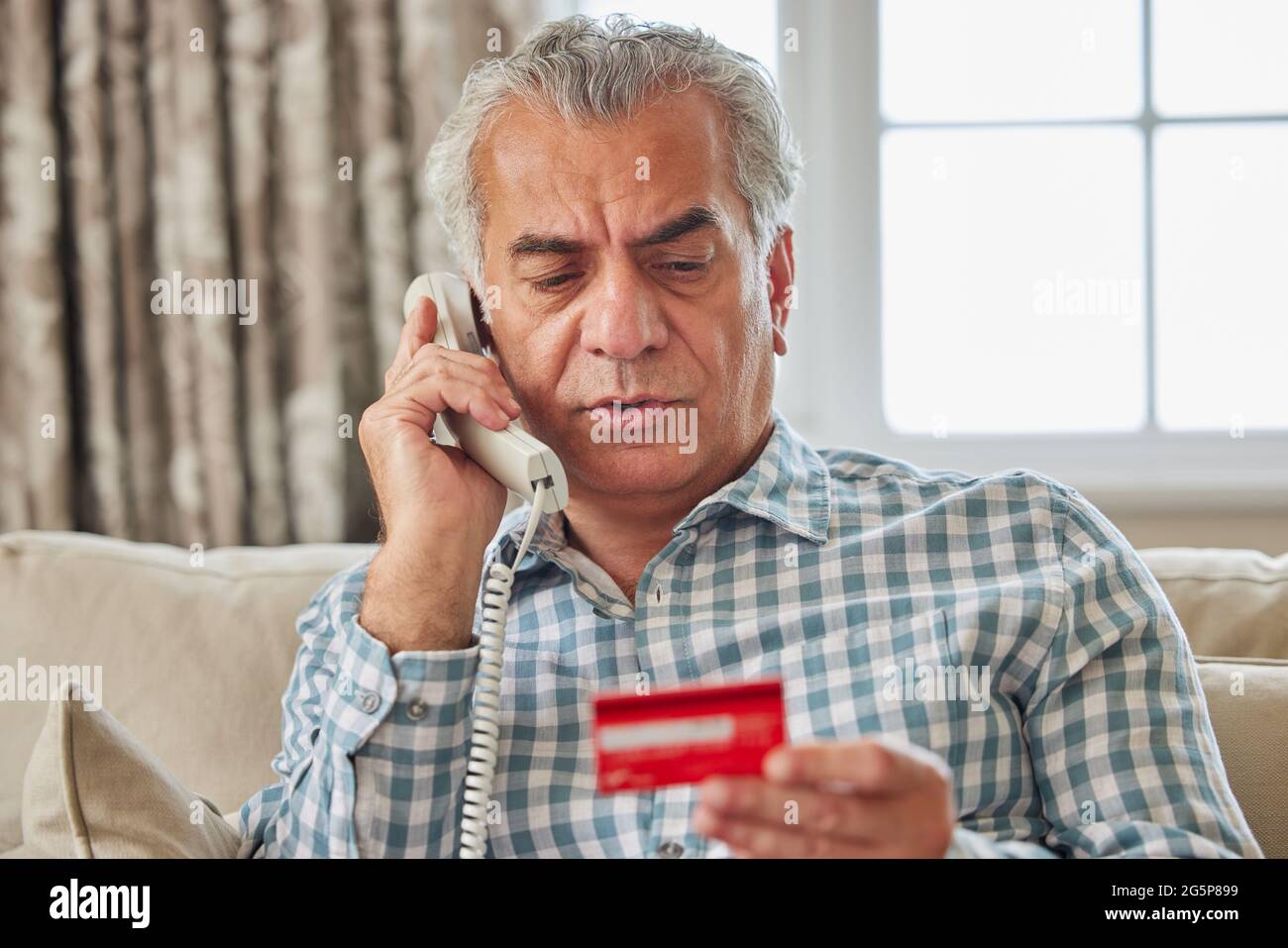 Uomo maturo a casa che fornisce i dettagli della carta di credito sul telefono Foto Stock