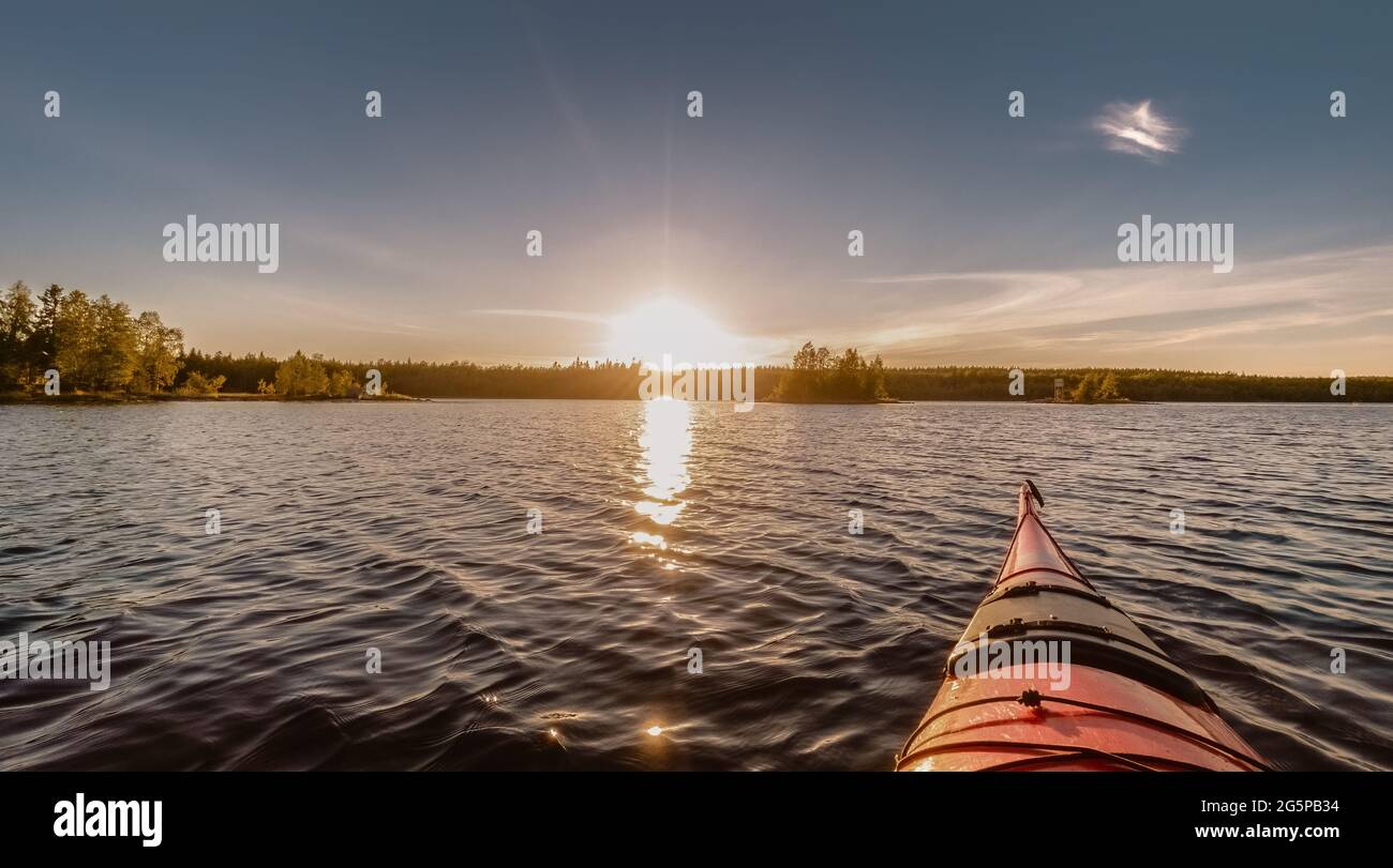 Kayak rossi in direzione della piccola isola e tramonto estivo al delta del fiume Umea, Svezia. Paesaggio scandinavo con pini e molta acqua. Umea, Swe Foto Stock