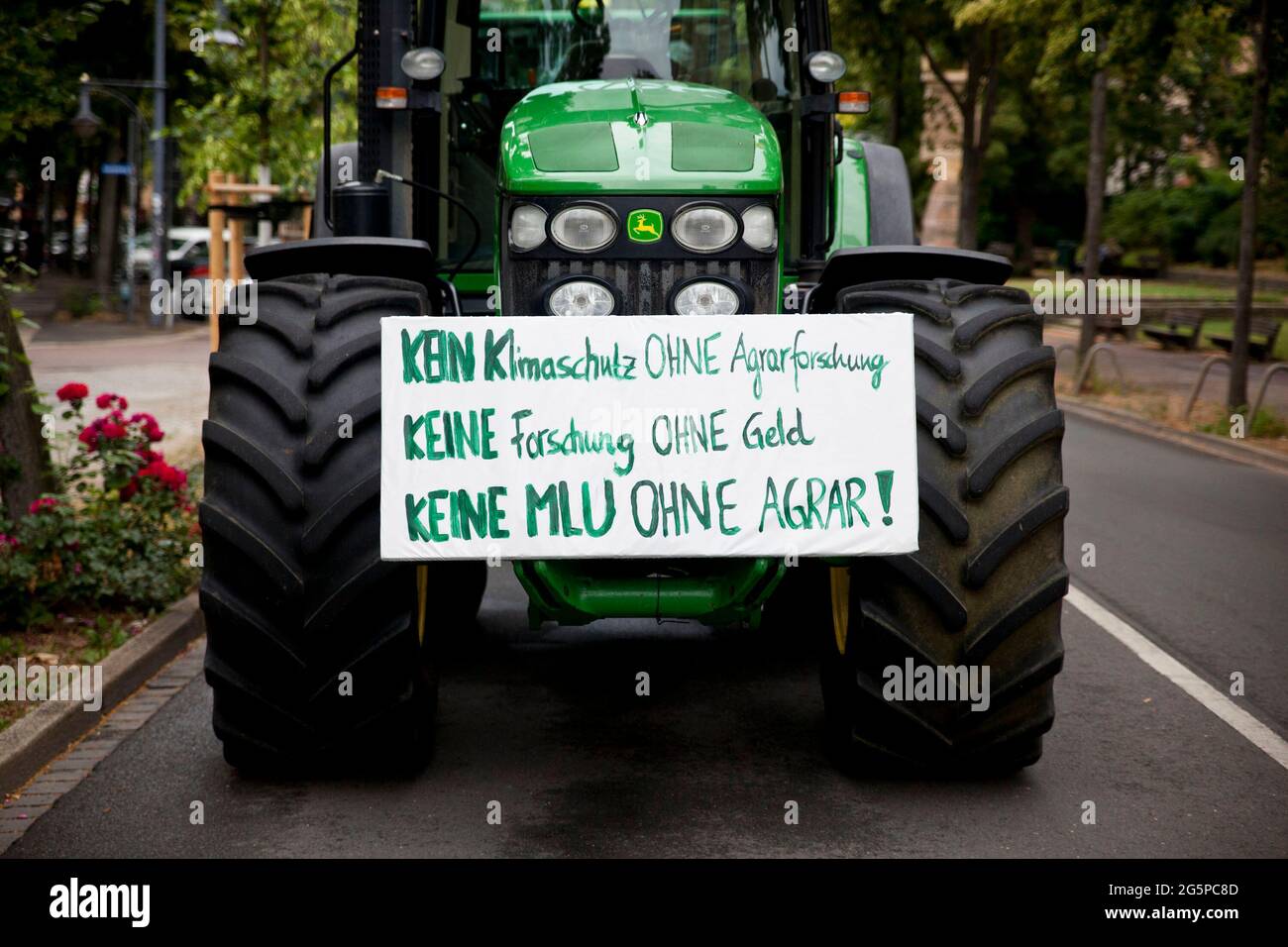 29 giugno 2021, Sachsen-Anhalt, Halle (Saale): Un trattore con un cartello che recita "Nessuna protezione del clima senza ricerca agricola" blocca la circonvallazione universitaria. Gli agricoltori della Sassonia-Anhalt e gli studenti dell'università (MLU) manifestano insieme contro i piani di tagli dell'università, che interesserebbero anche il Dipartimento di Scienze agricole. Foto: Johannes Stein/dpa-Zentralbild/dpa Foto Stock