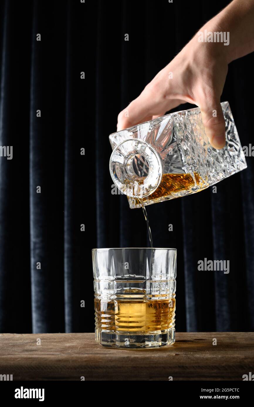 Versare whisky freddo in rocce su sfondo alla moda con tenda blu scuro. Formato verticale. Primo piano. Foto Stock