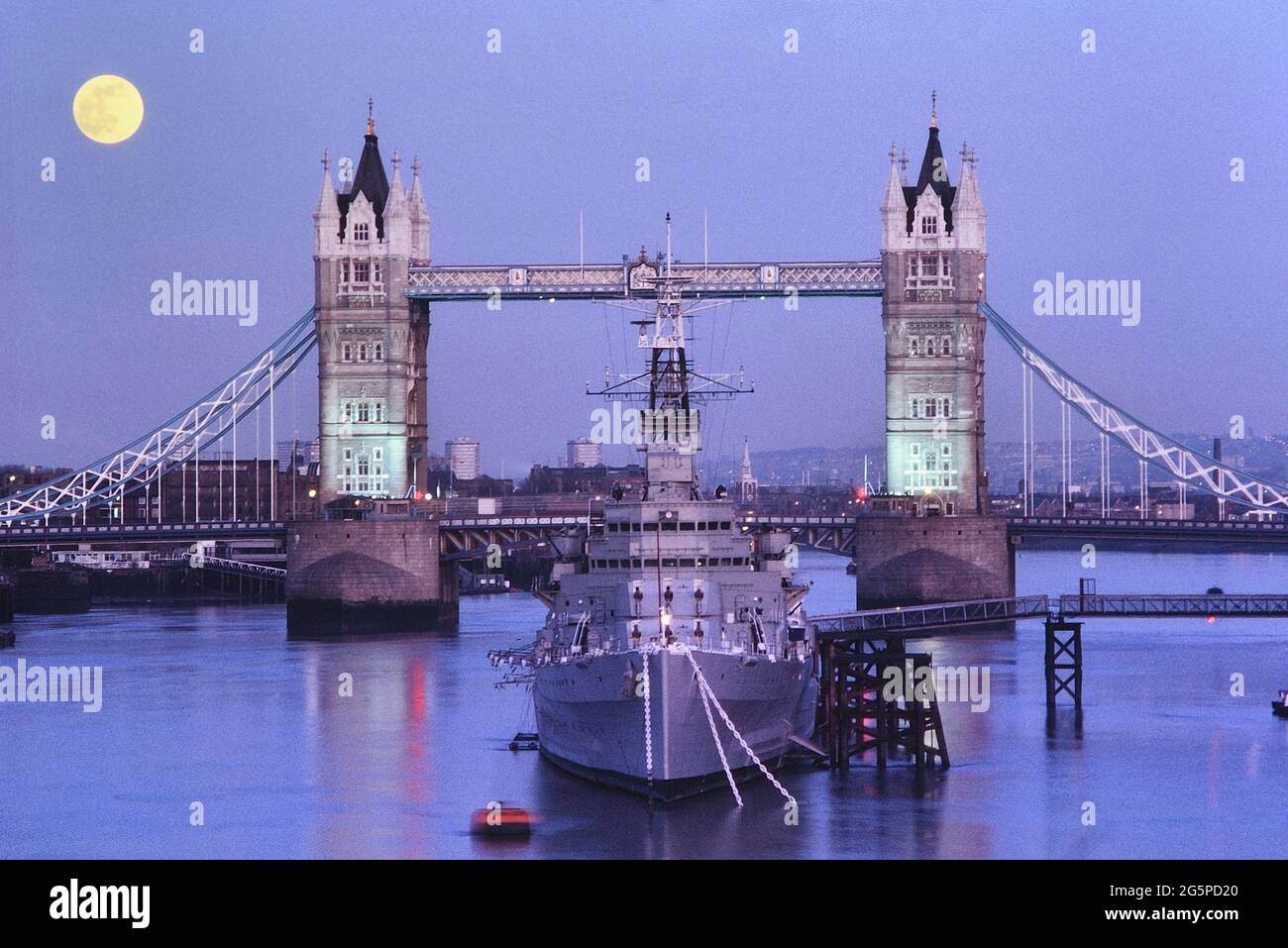 HMS Belfast ormeggiata sul Tamigi di fronte al Tower Bridge sotto una luna piena. Londra, Inghilterra, Regno Unito. Circa anni '80 Foto Stock