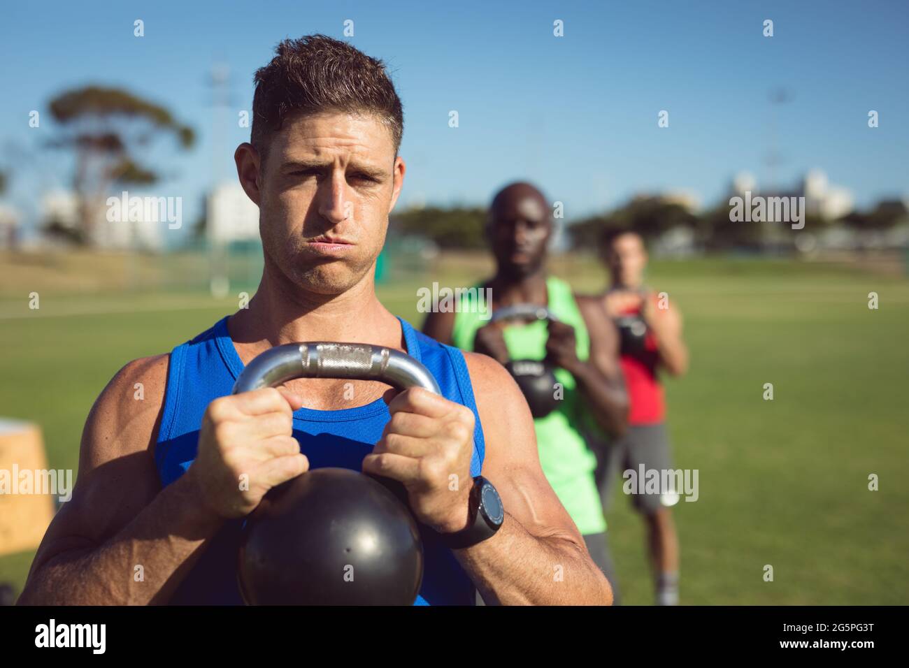 Diversi gruppi di uomini muscolosi che si allenano con le campane del bollitore all'aperto Foto Stock
