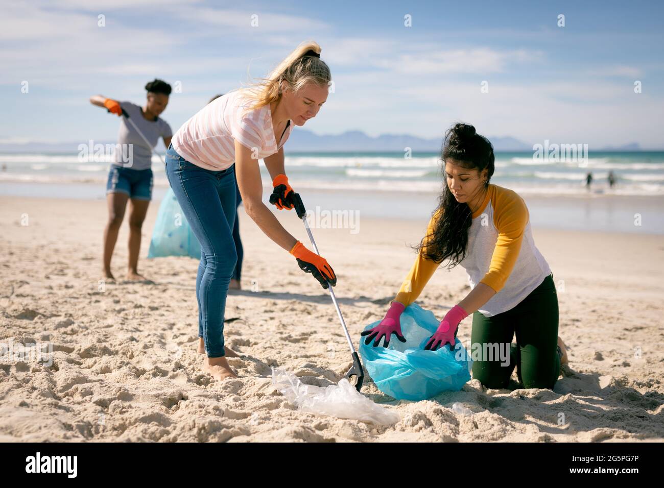 Gruppo vario di donne che camminano lungo la spiaggia, raccogliendo i rifiuti Foto Stock