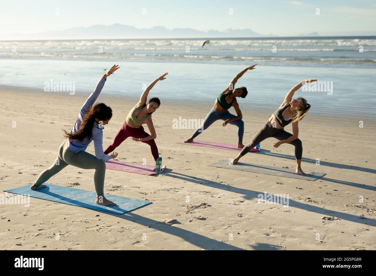 Gruppo vario di donne che praticano lo yoga, che si allungano in piedi sulla spiaggia Foto Stock