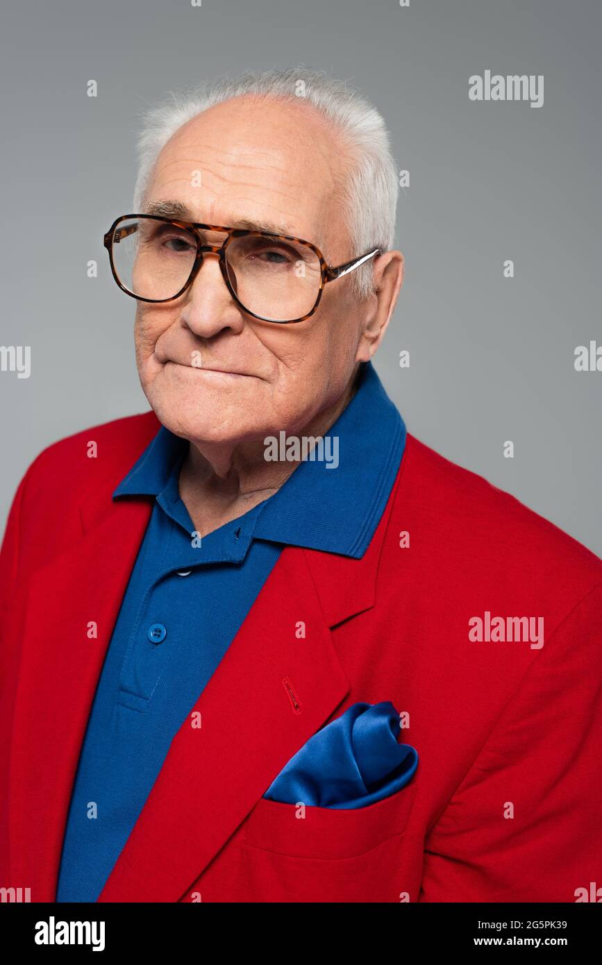 ritratto di un uomo anziano serio in blazer rosso e vetri isolati su grigio Foto Stock