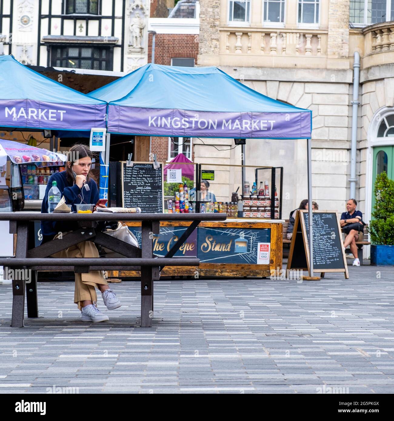 Kingston London UK, giugno 29 2021, Young Woman seduta da sola all'esterno su un banco di legno che mangia un pasto o un pranzo takeaway Foto Stock