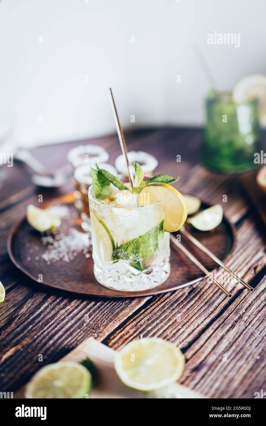 Foto luminosa di una bevanda fredda, un bicchiere di mojito con foglia di menta, ghiaccio, limone e zucchero su un tavolo di legno in stile retrò Foto Stock