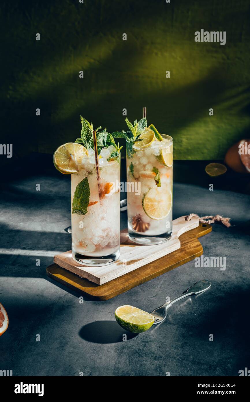 Fotografia scura di una bevanda fredda, un bicchiere di mojito con foglia di menta, ghiaccio, limone e zucchero su un tavolo di legno in stile vintage. Foto Stock