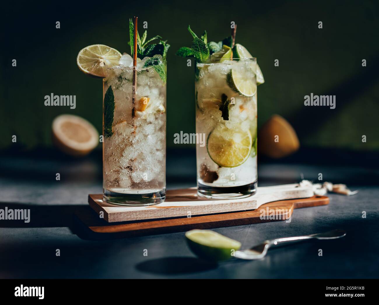 Fotografia scura di una bevanda fredda, un bicchiere di mojito con foglia di menta, ghiaccio, limone e zucchero su un tavolo di legno in stile vintage. Foto Stock