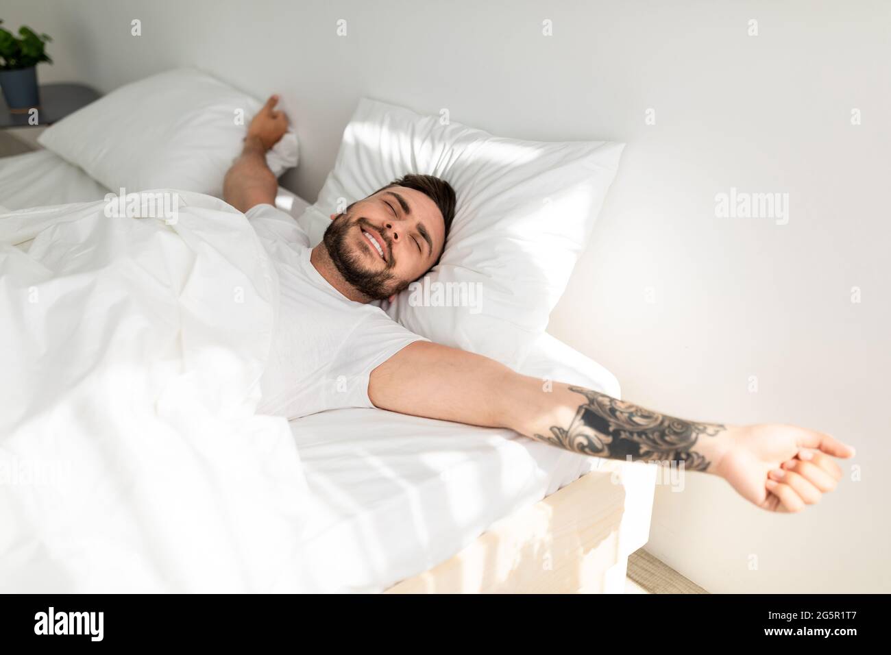 Sonno confortevole. L'uomo tatuato Wellslept si svegliò al mattino e si allunga le mani, sdraiato a letto Foto Stock