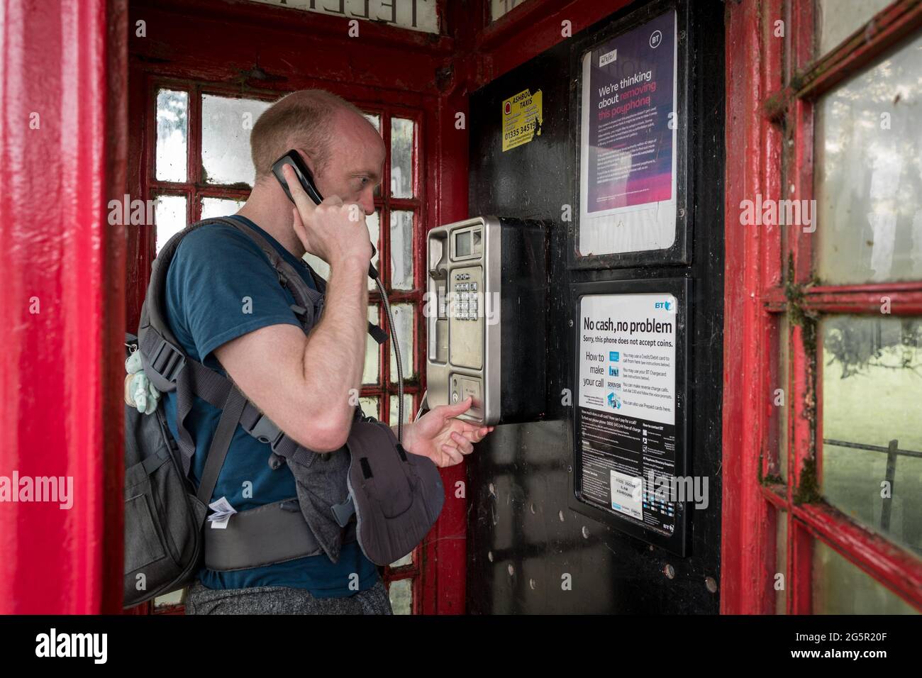 Uomo che effettua una chiamata utilizzando un ricevitore in una scatola telefonica rossa britannica. Foto Stock